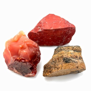 May include: Three rough, natural stones: a red jasper, a carnelian, and a tiger's eye. The stones are all different shapes and sizes, and they have a natural, unpolished look.