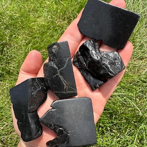 May include: Four black obsidian stones of varying shapes and sizes. The stones are smooth and polished, with a dark, glassy appearance.