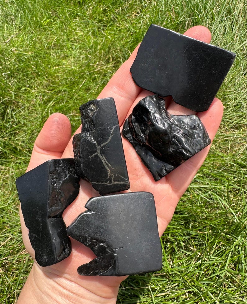 May include: Four black obsidian stones of varying shapes and sizes. The stones are smooth and polished, with a dark, glassy appearance.