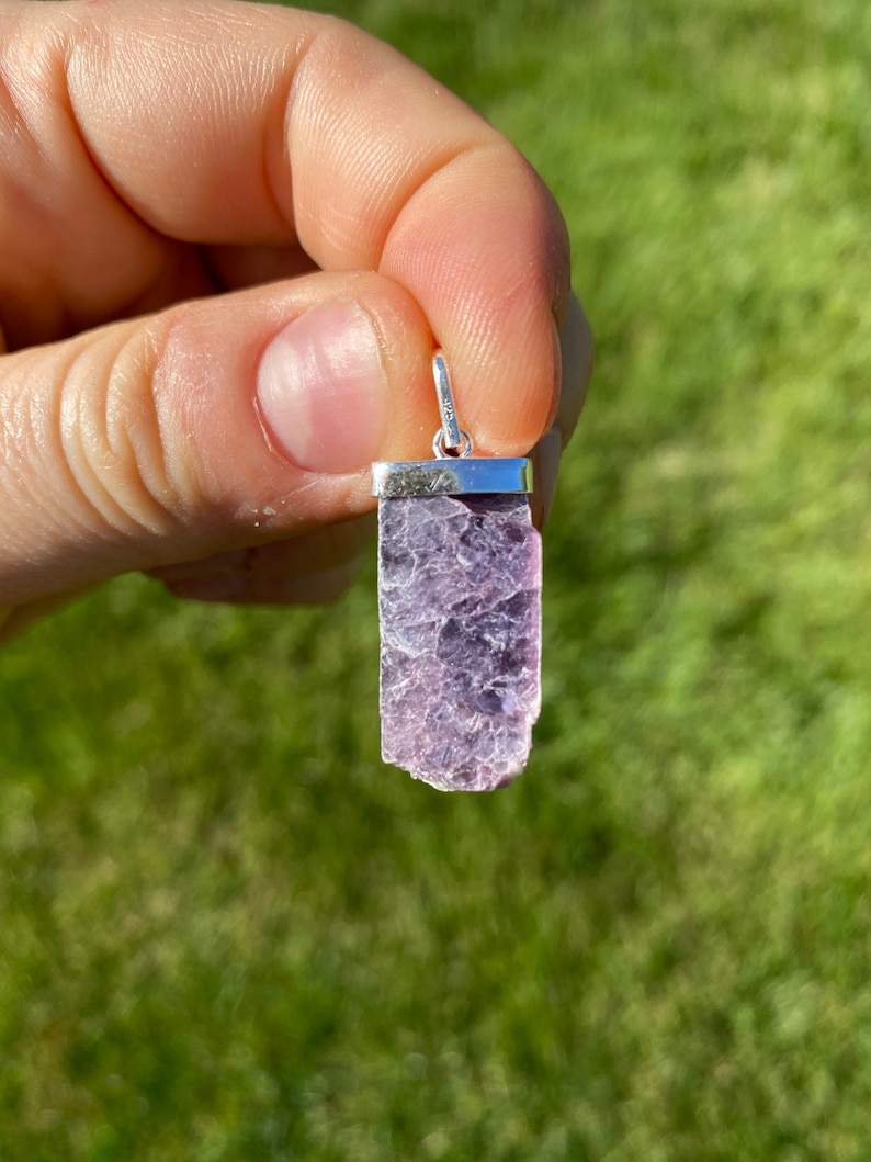 May include: A silver pendant featuring a raw, purple lepidolite crystal. The crystal is set in a silver bezel and hangs from a silver bail.