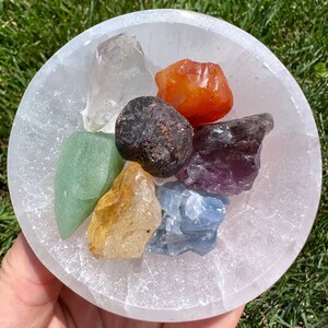 May include: A white selenite bowl filled with seven chakra crystals. The crystals are clear quartz, carnelian, garnet, amethyst, blue lace agate, citrine, and aventurine.