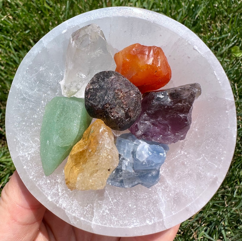 May include: A white selenite bowl filled with seven chakra crystals. The crystals are clear quartz, carnelian, garnet, amethyst, blue lace agate, citrine, and aventurine.