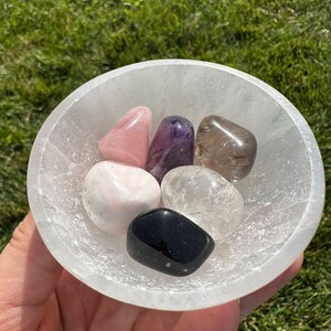 Puede incluir: Un cuenco de selenita blanco lleno de seis cristales pulidos: cuarzo rosa, amatista, cuarzo transparente, cuarzo ahumado, obsidiana negra y calcita blanca.