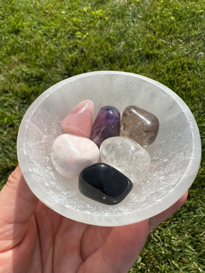 Puede incluir: Un cuenco de selenita blanco lleno de seis cristales pulidos: cuarzo rosa, amatista, cuarzo transparente, cuarzo ahumado, obsidiana negra y calcita blanca.
