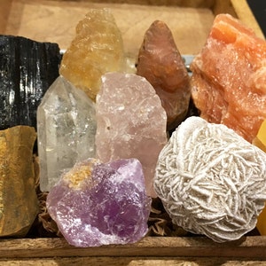 May include: A collection of ten polished crystals in a wooden box. The crystals include clear quartz, rose quartz, amethyst, tiger's eye, black tourmaline, selenite, and citrine.