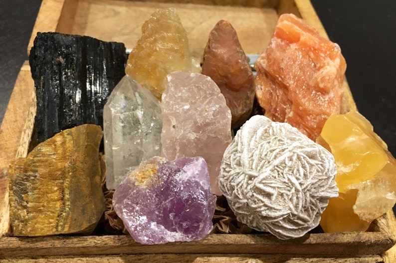 May include: A collection of ten polished crystals in a wooden box. The crystals include clear quartz, rose quartz, amethyst, tiger's eye, black tourmaline, selenite, and citrine.