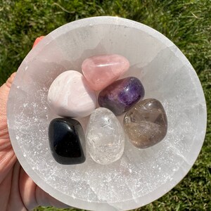 Puede incluir: Un cuenco de selenita lleno de seis cristales pulidos: cuarzo rosa, amatista, cuarzo transparente, cuarzo ahumado, calcita rosa y obsidiana negra.