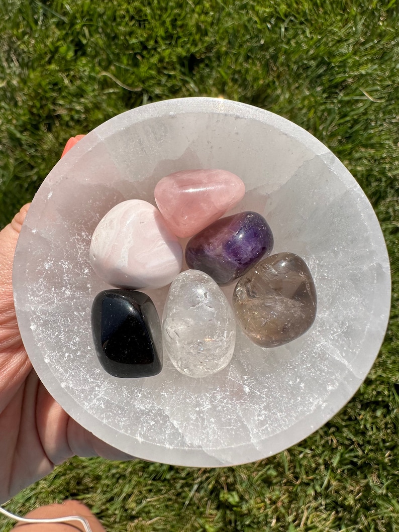 Puede incluir: Un cuenco de selenita lleno de seis cristales pulidos: cuarzo rosa, amatista, cuarzo transparente, cuarzo ahumado, calcita rosa y obsidiana negra.