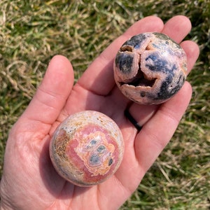 May include: Two pink and black patterned spheres made of polished stone. The spheres are about the size of a golf ball and have a smooth, rounded surface.