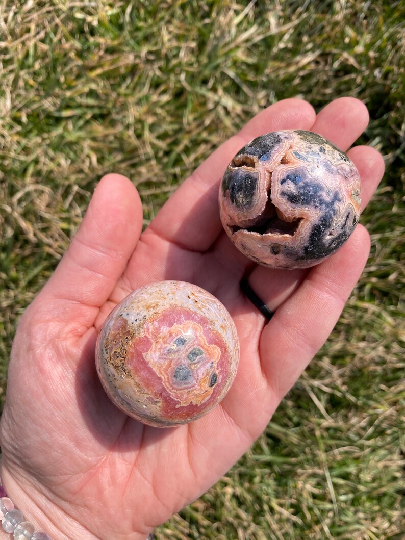 May include: Two pink and black patterned spheres made of polished stone. The spheres are about the size of a golf ball and have a smooth, rounded surface.