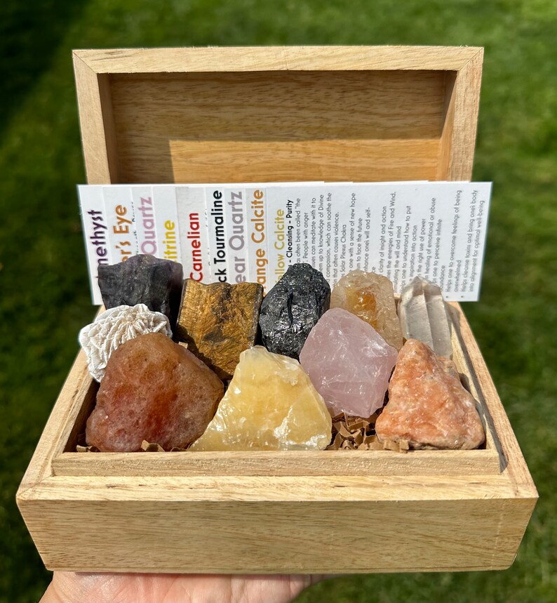 May include: A wooden box filled with various crystals and stones, including amethyst, tiger's eye, clear quartz, carnelian, black tourmaline, clear quartz, orange calcite, and yellow calcite. The box is open and the crystals are visible. The box is labeled with the names of the crystals.