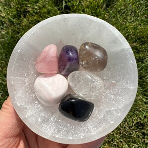 Puede incluir: Un cuenco de selenita lleno de seis cristales pulidos: cuarzo rosa, amatista, cuarzo ahumado, cuarzo transparente, obsidiana negra y calcita blanca.