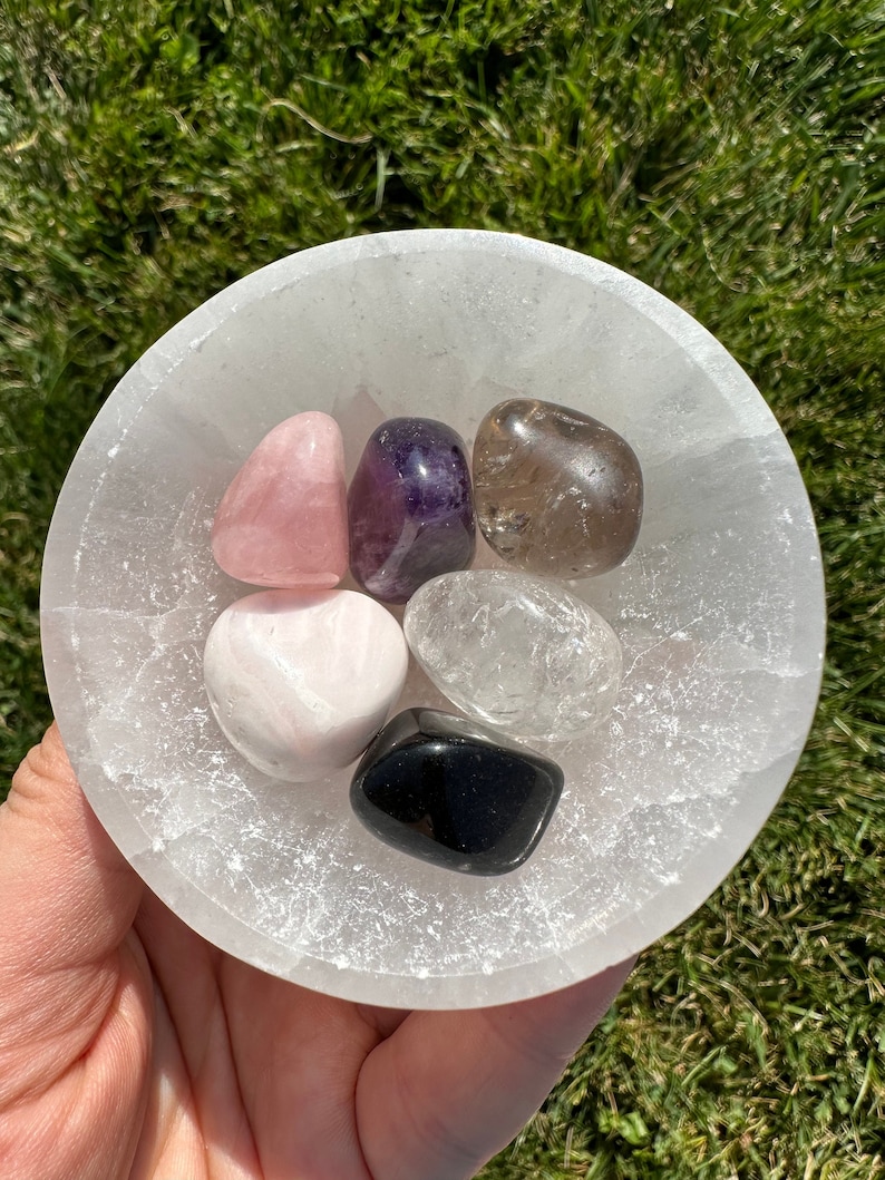 Puede incluir: Un cuenco de selenita lleno de seis cristales pulidos: cuarzo rosa, amatista, cuarzo ahumado, cuarzo transparente, obsidiana negra y calcita blanca.