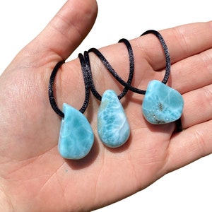 May include: Three teardrop-shaped blue and green gemstone pendants on black cords. The pendants are made of blue and green larimar.