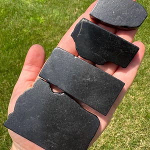 May include: Four black obsidian stones of varying sizes and shapes. The stones are smooth and polished.