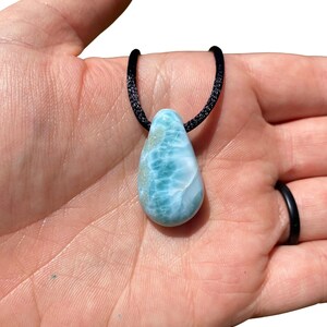 May include: A teardrop-shaped blue and green gemstone pendant on a black cord necklace.