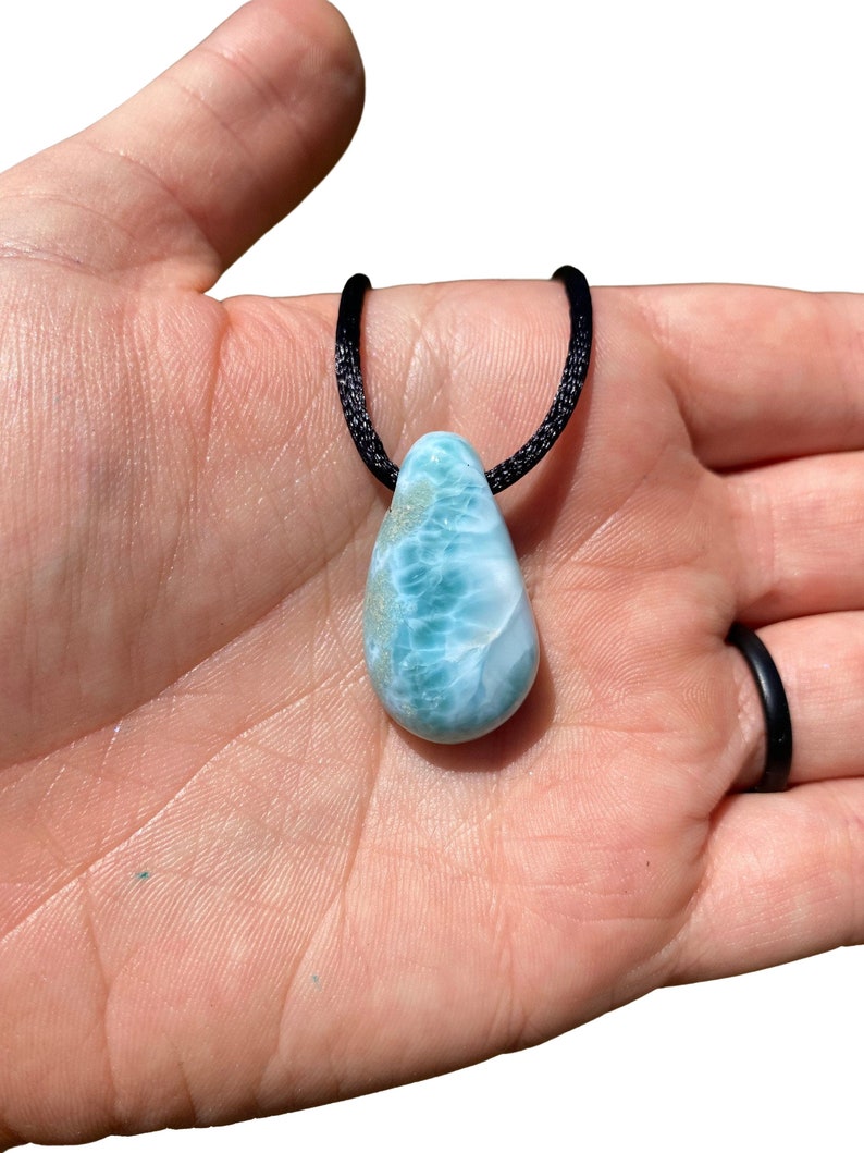 May include: A teardrop-shaped blue and green gemstone pendant on a black cord necklace.