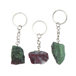 May include: Three silver keychains with different colored gemstone charms. The charms are green, red, and white, and are shaped like rough rocks.