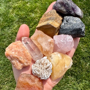 May include: A collection of ten tumbled and raw crystals, including amethyst, tiger's eye, rose quartz, clear quartz, calcite, selenite, and carnelian.