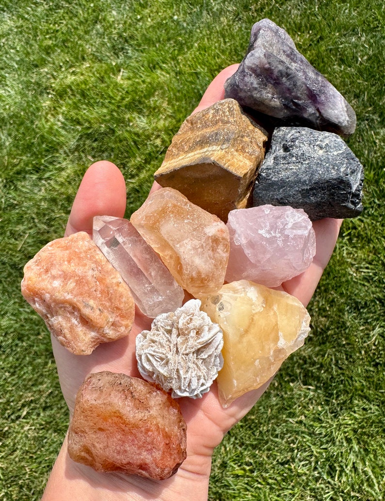 May include: A collection of ten tumbled and raw crystals, including amethyst, tiger's eye, rose quartz, clear quartz, calcite, selenite, and carnelian.