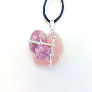 May include: A silver wire cage pendant with pink and purple crystals. The pendant is on a black cord.