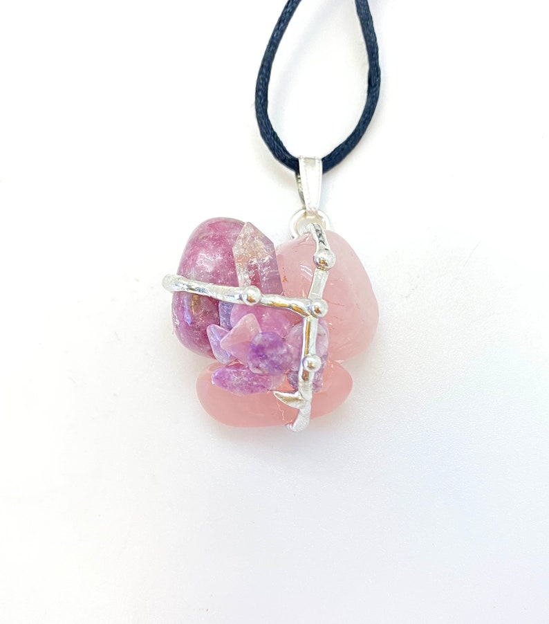 May include: A silver wire cage pendant with pink and purple crystals. The pendant is on a black cord.