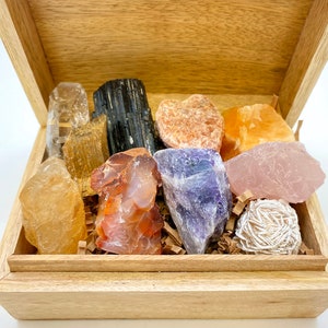 May include: A wooden box filled with a variety of crystals and stones, including clear quartz, amethyst, rose quartz, citrine, and carnelian.