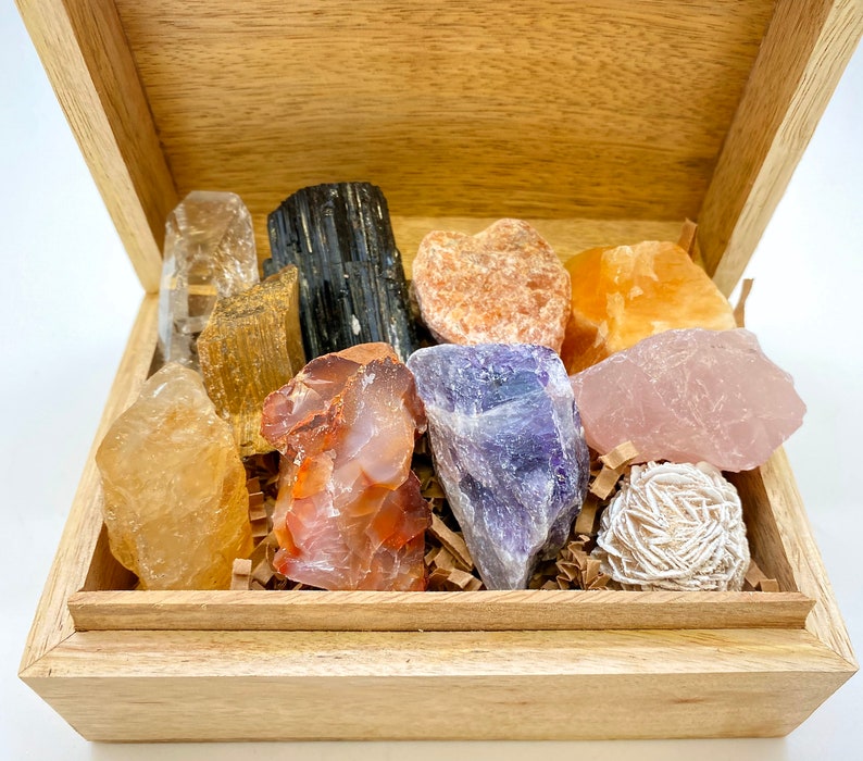 May include: A wooden box filled with a variety of crystals and stones, including clear quartz, amethyst, rose quartz, citrine, and carnelian.