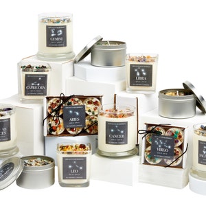 May include: Assortment of zodiac-themed candles in glass jars and tin containers. The candles are arranged on white boxes and feature the constellations and names of each zodiac sign: Aries, Taurus, Gemini, Cancer, Leo, Virgo, Libra, Scorpio, Sagittarius, Capricorn, Aquarius, and Pisces.