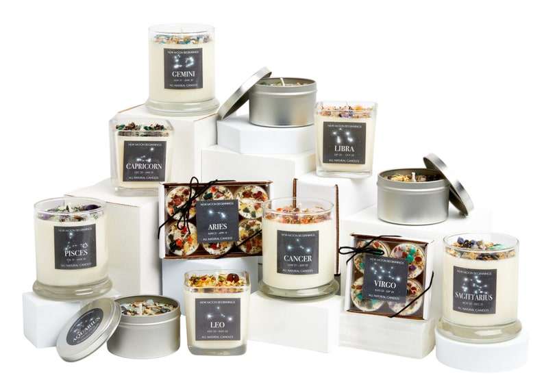 May include: Assortment of zodiac-themed candles in glass jars and tin containers. The candles are arranged on white boxes and feature the constellations and names of each zodiac sign: Aries, Taurus, Gemini, Cancer, Leo, Virgo, Libra, Scorpio, Sagittarius, Capricorn, Aquarius, and Pisces.