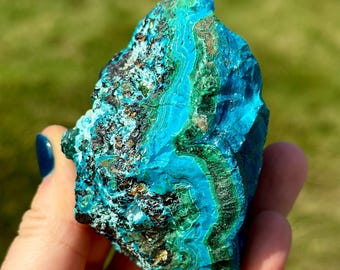 May include: A large, rough, blue and green gemstone with a layered, banded pattern. The gemstone is a raw, natural specimen of azurite and malachite.