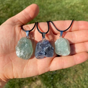 Puede incluir: Tres colgantes de cristal en cordones negros. Los colgantes son verde claro, verde oscuro y azul oscuro. Los cristales son todos &aacute;speros y naturales.