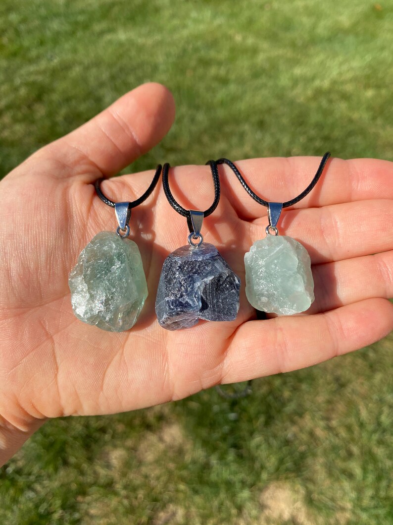 Puede incluir: Tres colgantes de cristal en cordones negros. Los colgantes son verde claro, verde oscuro y azul oscuro. Los cristales son todos &aacute;speros y naturales.