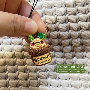 May include: A small crocheted Mandrake plant keychain with a brown pot and green leaves. The pot has a yellow label that reads "MANDRAKE CAUTION".