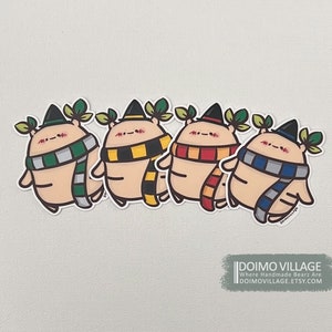 May include: Four cartoon stickers of round, tan creatures wearing black hats, scarves, and leaf accents. The scarves are green and gray, yellow and black, red and orange, and blue and gray. The stickers are on a white background.