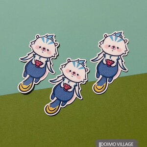 Pu&ograve; includere: Tre adesivi di orsi cartoon blu e bianchi con piedi gialli e una fragola rossa nelle loro zampe. Gli adesivi sono su uno sfondo verde e blu. Il testo "DOIMO VILLAGE" &egrave; nella parte inferiore dell'immagine.