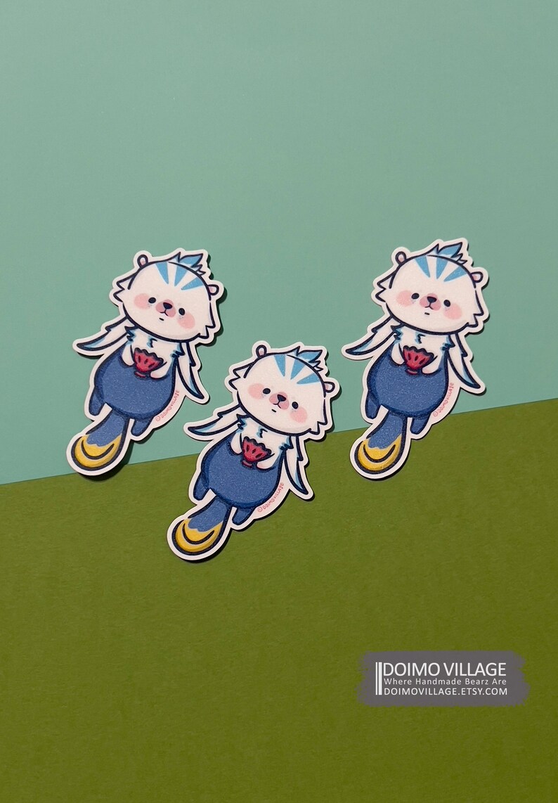 Pu&ograve; includere: Tre adesivi di orsi cartoon blu e bianchi con piedi gialli e una fragola rossa nelle loro zampe. Gli adesivi sono su uno sfondo verde e blu. Il testo "DOIMO VILLAGE" &egrave; nella parte inferiore dell'immagine.