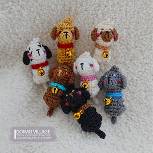 May include: A collection of eight crocheted dog plushies in various colors, including white, brown, black, and gray. Each plush has a bell attached to its collar.