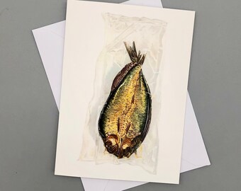 May include: A smoked fish, possibly a herring, is packaged in a clear plastic bag. The fish is golden brown and has a green hue. The fish is on a white background.