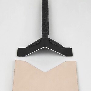 May include: A black leather crafting tool with a V-shaped metal blade and a handle. The tool is used to create a V-shaped cut in leather.