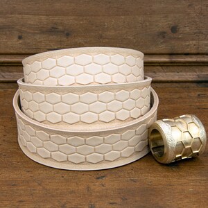May include: Three stacked leather belt straps with a hexagonal pattern and a brass buckle with a hexagonal pattern.