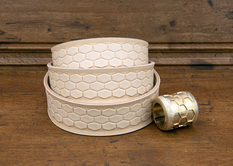 May include: Three stacked leather belt straps with a hexagonal pattern and a brass buckle with a hexagonal pattern.