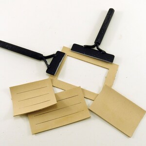 May include: Two black metal tools with handles and a flat blade, used for scraping or smoothing surfaces. The tools are lying on a white surface with four pieces of brown cardboard with lines on them.