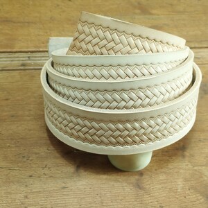 May include: A close-up of a stack of off-white leather straps with a woven pattern. The straps are rolled up and have a decorative edge.