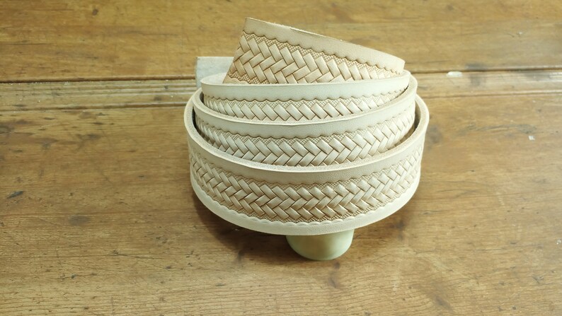 May include: A close-up of a stack of off-white leather straps with a woven pattern. The straps are rolled up and have a decorative edge.