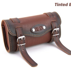 May include: Tinted brown leather motorcycle saddlebag with two buckles and a metal plate with the initials "R.S." embossed on it.