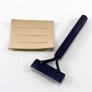 May include: A blue leather working tool with a handle and a blade. The tool is used to score leather. A piece of brown leather with lines scored into it is also shown.
