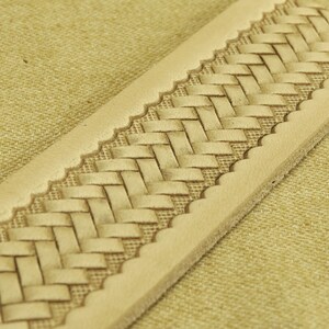 May include: A close-up of a light brown leather strap with a woven pattern. The strap has a scalloped edge.