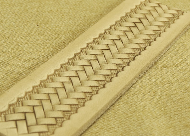May include: A close-up of a light brown leather strap with a woven pattern. The strap has a scalloped edge.