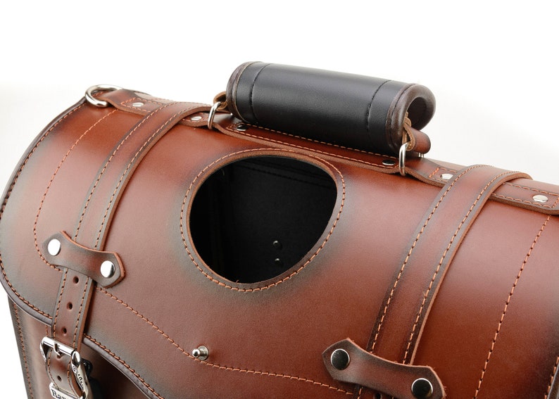 Puede incluir: Una alforja de moto de cuero marr&oacute;n con un asa de cuero negro y una abertura cosida. La bolsa tiene un cierre de hebilla y detalles met&aacute;licos.